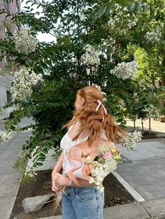 a woman with red hair is standing on the sidewalk and has flowers in her hand