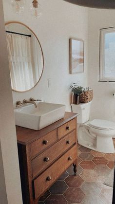 a bathroom with a toilet, sink and mirror in it's corner next to a window