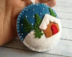 a hand holding a felt ornament with a house on it