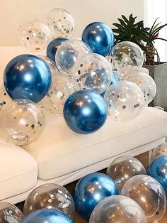 blue and silver balloons are on the floor in front of a white couch with a potted plant