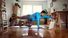 a woman in blue shirt doing yoga on wooden floor next to table and laptop computer