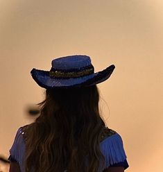 a woman in a blue dress and hat is looking at the sky with her back to the camera