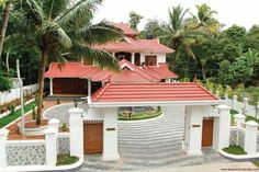 the house is surrounded by palm trees and white fenced in area with red tiled roof