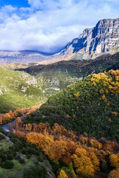 the valley is surrounded by mountains and trees with yellow, green, and orange leaves