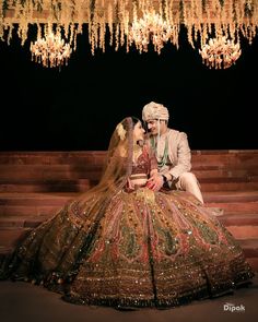 a bride and groom sitting on steps in front of chandelier with lights hanging from the ceiling