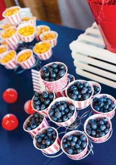 blueberries are arranged in small cups on a table with red and white striped buckets