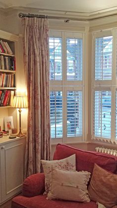 a living room filled with furniture and windows covered in shuttered curtains, along with bookshelves