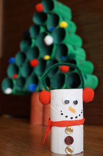 a toilet paper roll snowman next to a small christmas tree with ornaments on it