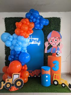 a birthday decoration with balloons and construction vehicles on the grass in front of a wall