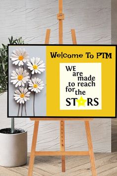 a welcome sign with daisies on it in front of a potted plant and wooden easel