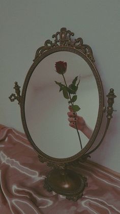 a person is holding a rose in front of a round mirror on a pink table cloth