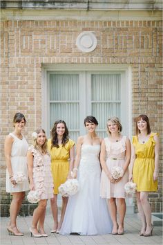 a group of women standing next to each other in front of a brick building holding bouquets