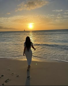 a woman walking on the beach at sunset