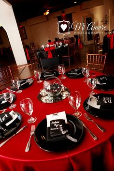 a red table cloth with black plates and silverware is set for a formal dinner