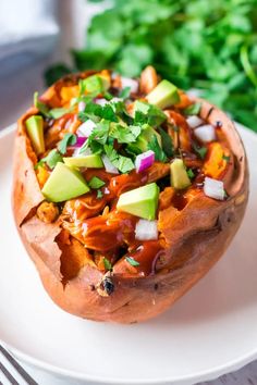 a baked sweet potato is topped with avocado, cilantro and red onion