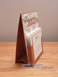 a card holder with a calendar on it sitting on top of a wooden table in front of a gray wall