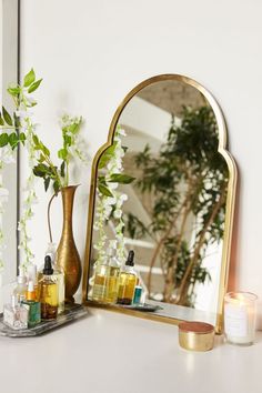 a mirror and some bottles on a table next to a vase with flowers in it