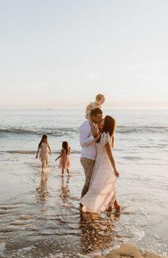 a man and woman hug while standing in the water at the beach with their children