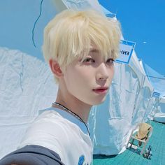 a young man with blonde hair standing in front of a white tent and blue sky