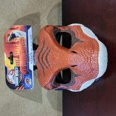 an orange plastic mask sitting on top of a table next to a package of toothpaste