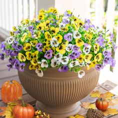 a large pot filled with lots of flowers next to pumpkins and acorns