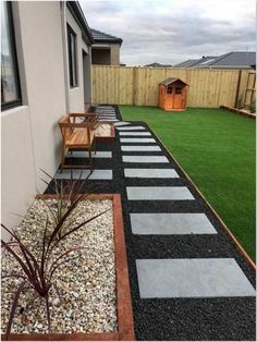 a small backyard with grass, gravel and wooden benches on the side of the house