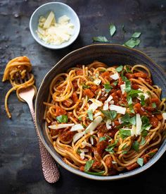 a bowl of spaghetti with meat and parmesan cheese on the side next to two spoons