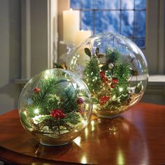 two glass balls filled with christmas decorations on top of a table next to a candle