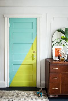 a blue and yellow door in a room with a mirror on the wall next to it