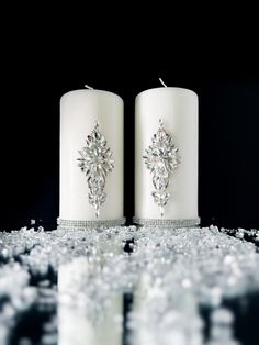 two white candles sitting next to each other on top of snow covered ground with crystals