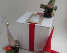 two little gnomes are sitting on top of a present box and one is holding a pine cone