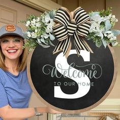 a woman standing in front of a welcome sign with flowers and a bow on it