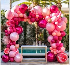 an arch made out of balloons and pinks next to a pool with palm trees