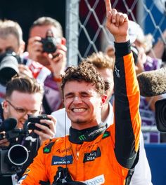 a man in an orange racing suit waves to the crowd while holding his hand up