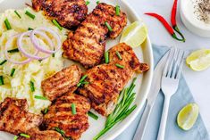 grilled chicken with mashed potatoes and onions on a white plate next to silverware