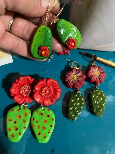 a person is holding some green and red earrings on a blue table next to other items