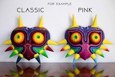 two paper masks with spikes on them are sitting next to each other, one is pink and the other is green