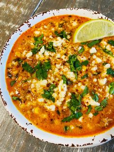 a white bowl filled with soup and garnished with cheese, cilantro and lime