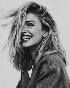 a black and white photo of a woman with her hair blowing in the wind, smiling