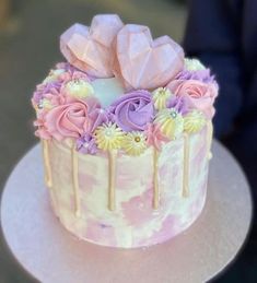 a white cake with flowers and icing on it sitting on a plate in front of a person