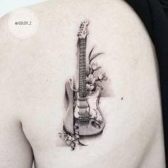 a woman's back with a guitar tattoo on her left shoulder and flowers growing out of it