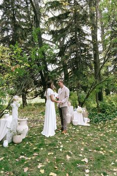 a bride and groom are standing in the grass at their outdoor wedding ceremony, surrounded by trees