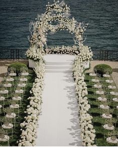 an outdoor ceremony setup with white flowers and greenery on the grass, overlooking the water