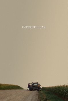 two people standing next to an old truck on the side of a dirt road in front of a corn field