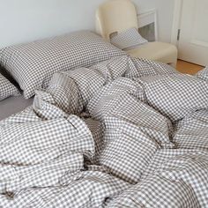 an unmade bed sitting on top of a wooden floor next to a white chair