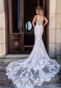 a woman standing in front of a door wearing a wedding dress with an open back