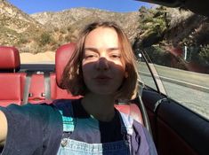 a woman sitting in the driver's seat of a car with mountains in the background