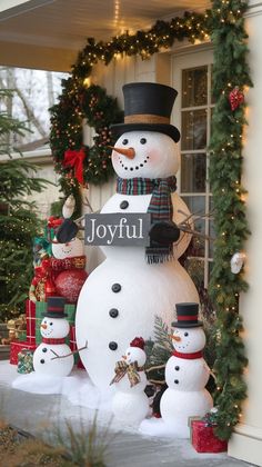 a large snowman and two small snowmen in front of a house with christmas decorations