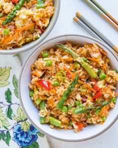 two bowls filled with rice and veggies next to chopsticks on a table