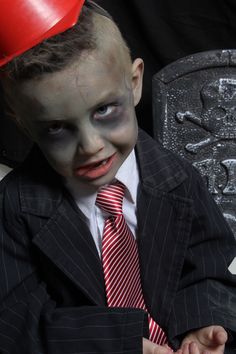 a young boy dressed up in a suit and tie with blood on his face wearing a red hat